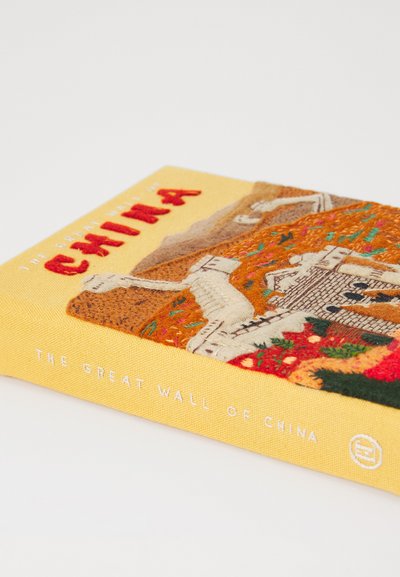 Un livre à couverture rigide jaune intitulé "La Grande Muraille de Chine" avec une broderie texturée représentant le mur et le paysage environnant.