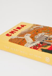 Livre à couverture rigide intitulé "La Grande Muraille de Chine", avec une couverture jaune texturée ornée d'éléments de design brodés et de lettres blanches.