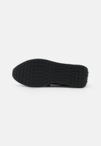 Black rubber shoe sole with rounded studs for traction. Features a textured surface and a subtle logo imprint near the heel.