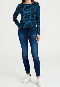 Top negro de manga larga con patrón floral azul, combinado con jeans ajustados azules y zapatillas blancas. Textura suave y diseño casual.