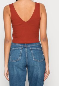 Débardeur côtelé de couleur rouille avec un col en V, porté avec un jean bleu taille haute doté de poches arrière et d'une texture en denim.