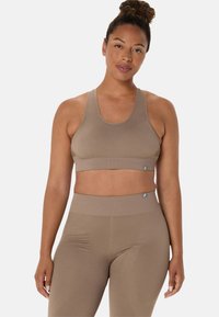 Ruskea urheiluliivi ja korkeavyötäröiset legginsit sileästä, ribatusta kankaasta, joka istuu tiiviisti. Koristeena logoelementtejä ja minimalistinen muotoilu.
