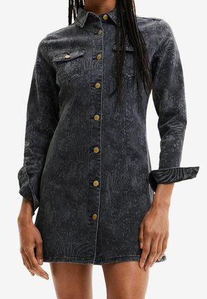 Langarmige zwarte denimjurk met subtiele dierenprint, gouden knopen aan de voorkant, borstzakken, gedragen door een persoon met gevlochten haar en opgerolde mouwen.