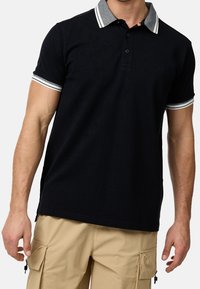 Schwarzes Poloshirt mit grauem gestreiften Kragen, Drei-Knopf-Leiste und gerippten Bündchen; glattes Material; dezentes Logo auf der Brust.