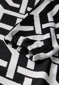 Schwarz-weiß gemusteter Stoff mit geometrischen Designs. Der Stoff hat eine weiche Textur und verfügt über ein gerafftes elastisches Bündchen.