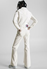 Chaqueta de mezclilla blanca y pantalones acampanados con un acabado texturizado. Presenta un parche con logo en la parte trasera de la cintura y bolsillos laterales.