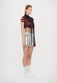 Top corto de manga corta negro y multicolor con detalles de flecos, combinado con una mini falda blanca y zapatillas blancas. Textura de tela lisa.