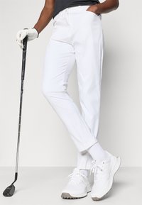 Bijele golf hlače od glatkog, laganog materijala. Imaju klasičan kroj s džepovima, uparene s bijelim sportskim cipelama i rukavicama.