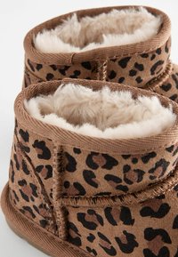 Leopardmönstrade ankelstövlar i brunt, med mjukt beige fuskpälsfoder och sydda detaljer, samt en strukturerad ytfinish.