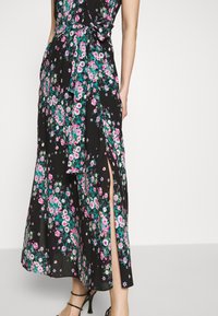 Svart blommig maxiklänning med ett livfullt mönster av rosa, vita och gröna blommor, med en hög slits och ett band i midjan.