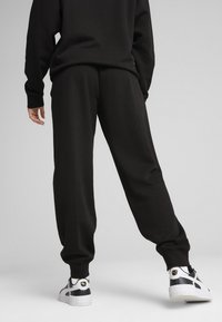 Juoda sportinė kelnė, pagaminta iš minkštos medžiagos, pasižyminti laisvu modeliu, elastinga juosmens juosta ir rankogaliais. Sukomponuota su juodais ir baltais sportbačiais.