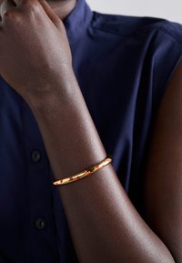 Personne à la peau foncée portant une chemise sans manches bleu marine et un bracelet en or avec des taches rouges sur le poignet.