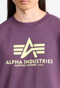 Purple cotton sweatshirt featuring a large yellow graphic with the letters "A" and horizontal stripes; text reads "ALPHA INDUSTRIES, KNOXVILLE, TENNESSEE, U.S.A."