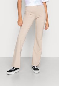 Beige flare broeken van rekbare stof, met een hoge taille en een gladde, strakke textuur. Gecombineerd met zwart-witte veterschoenen.