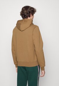 Brun huva sweatshirt med ribbad nederkant. Mjukt tyg, avslappnad passform och en enkel design. Åtföljs av gröna byxor med sidostråk.