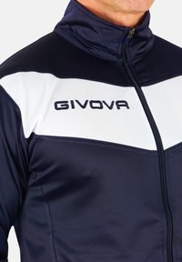 Jachetă sport de culoare bleumarin, cu un panou alb în zona pieptului, având un guler înalt și închidere cu fermoar. Logo-ul "GIVOVA" în negru pe partea stângă sus.