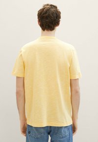 Camiseta amarilla de manga corta con una textura suave, que presenta un cuello redondo y un corte ligeramente relajado. La vista trasera muestra un diseño simple y sin adornos.