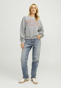 Felpa grigia con grafica rossa "NEW YORK", abbinata a jeans azzurri e sneaker bianche con accenti verdi e rossi.