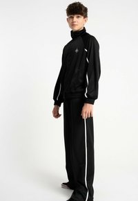 Czarny dres składający się z kurtki zapinanej na zamek z wysokim kołnierzem oraz białymi paskami po bokach, w zestawieniu z dopasowanymi spodniami. Gładka tekstura.