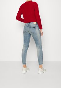 Jeans ajustados de mezclilla azul con un ajuste de tiro medio, combinados con un suéter de punto rojo. El conjunto presenta un lavado claro, un ligero desvanecimiento y bolsillos traseros.