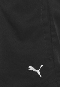 Pantalones cortos de tela negra con un logo blanco de Puma. Material texturizado con detalles de costura visibles y un bolsillo lateral.