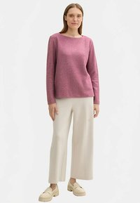 Rózsaszín, hosszú ujjú felső kerek nyakkivágással, világos színű, bőszárú nadrággal és bézs platform cipővel párosítva. Simas textúra.