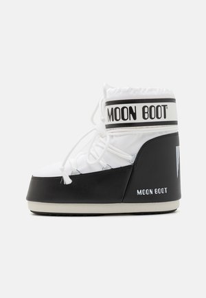 Hvit og svart snøstøvel med rund tå, snøring foran, polstret ankel, og "MOON BOOT" merkevare på kanten og siden.