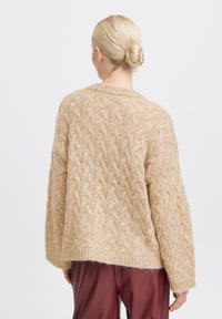 Virkattu bežsweater med tekstuuri, kabelmønster, oversized passform, brede ærmer og ribbet kant, parret med bordeaux bukser.