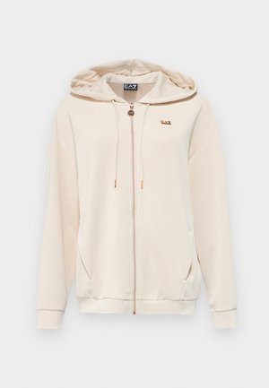 Sudadera con cremallera beige, con un bolsillo frontal, capucha con cordón y un pequeño logo dorado. Tejido suave con una textura lisa y un ajuste relajado.