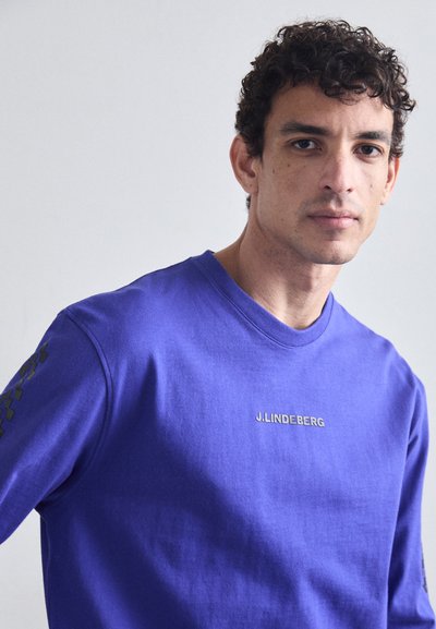 Sweat-shirt violet à manches longues en coton, doté d'un col rond et d'un logo sur la poitrine, avec des accents de motifs géométriques sur les manches.