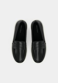 Μαύρα δερμάτινα loafers χωρίς κορδόνια με λευκές σόλες, σε θέα από πάνω, με διακοσμητικό λουράκι στο επάνω μέρος και ενθέματα με το λογότυπο.