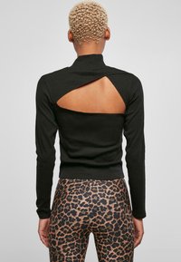 Svart langermet topp med et design som har utskjæring på ryggen, laget av et glatt stoff. Brukt med leopardmønstrede tights.