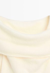 Tissu en tricot crème clair avec une texture lisse, doté d'un col replié et d'une drapé doux. Aucune motif visible ni détail de quincaillerie.