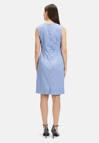 Ärmelloses blaues Kleid mit floralem Muster, tailliertem Rücken, knielangem Saum und einem Schlitz. Kombiniert mit schwarzen High-Heels.