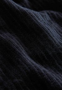 Svart strukturerad tyg med ett vågigt mönster, som har fin ribbning och en mjuk, plyschig yta som subtilt reflekterar ljus.