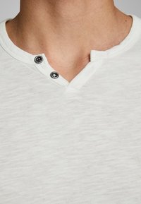 Lichtgrijs henley-shirt met een gestructureerde stof, twee zwarte knopen en een V-halsontwerp voor extra detail.