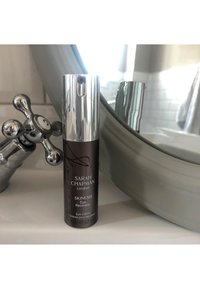 Flasche von Sarah Chapmans Skinesis Eye Recovery Cream auf dem Waschbecken im Badezimmer, nahe einem traditionellen verchromten Wasserhahn und Spiegel.