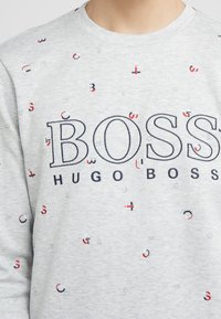 Felpa grigia a girocollo con la scritta "BOSS HUGO BOSS" in grandi lettere blu navy, con piccoli accenti grafici rossi e blu distribuiti in modo sparso.