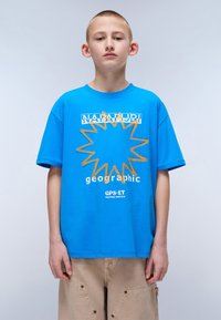 Blue cotton t-shirt featuring a yellow sunburst design, logo text, and relaxed fit. Paired with beige cargo shorts with snap pockets.