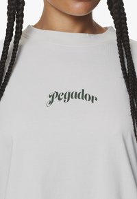 Ljust grå sweatshirt med texten "pegador" i mörkgrön kursiv stil på framsidan. Mjuk, slät textur med en avslappnad passform.