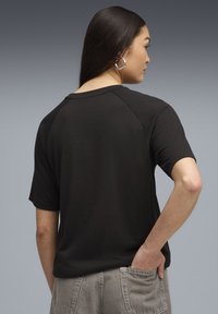 Sort kortærmet T-shirt med rund halsudskæring og raglanærmer. Bemærk den glatte tekstur og den afslappede pasform, kombineret med grå høj taljede bukser.