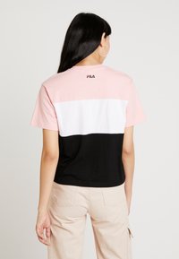 Camiseta de manga corta en bloque de colores rosa, blanca y negra, con cuello redondo y pequeño logo de FILA en la parte superior de la espalda. Material de algodón suave.