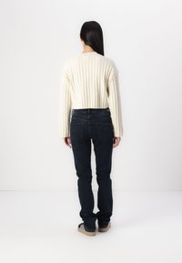 White ribbed sweater, cropped design, paired with dark blue jeans. Shoes feature a gum sole and black base with white stripes.
