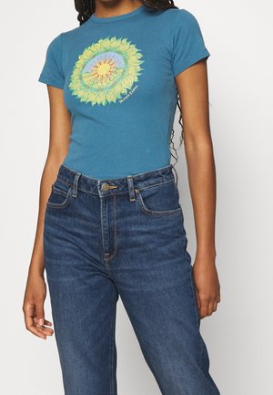 Tiefgrünes Baumwoll-T-Shirt mit einem bunten Sonnenblumen-Grafik in der Mitte, kombiniert mit hoch taillierten blauen Denim-Jeans, die einen klassischen Stil präsentieren.