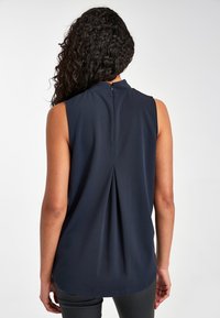 Sleeveless navy blouse with a high collar, keyhole back closure, and a pleated detail at the center back. Smooth, lightweight fabric.