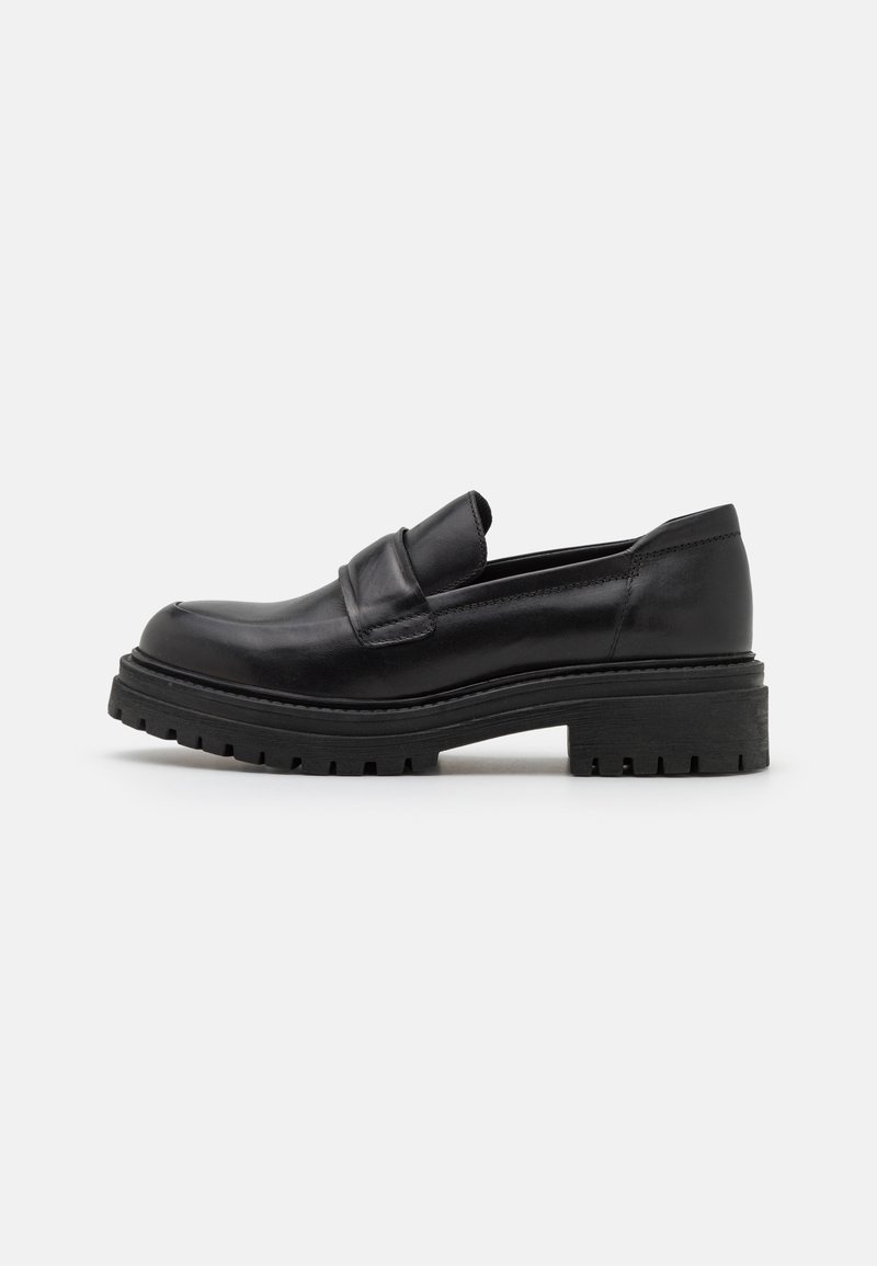 Mocassin en cuir noir avec semelle crantée épaisse et petit talon, vue de côté sur fond clair uni.