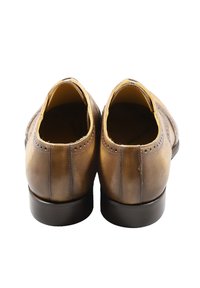 Scarpe in pelle marrone con una texture liscia, punta arrotondata, tacco basso e cuciture decorative lungo la tomaia, caratterizzate da un design brogue.