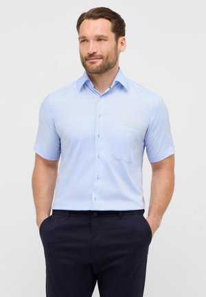 Kurzarm-Hemd aus hellblauem Stoff mit einer Brusttasche, weißen Knöpfen und einem leicht strukturierten Kragen. Kombiniert mit dunklen Hosen.