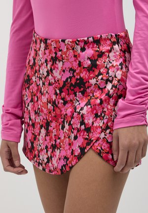 Jupe mini florale avec des nuances de rose et de rouge sur fond noir. Tissu doux, design croisé et couture visible à la taille.