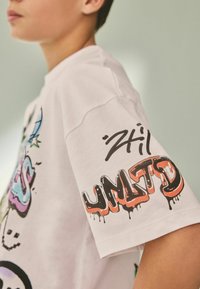 Bijela pamučna majica s grafičkim motivima u stilu grafita u živim bojama na tijelu i rukavima, s natpisima "241" i "UMTD" u podebljanom, kapljajućem tekstu.
